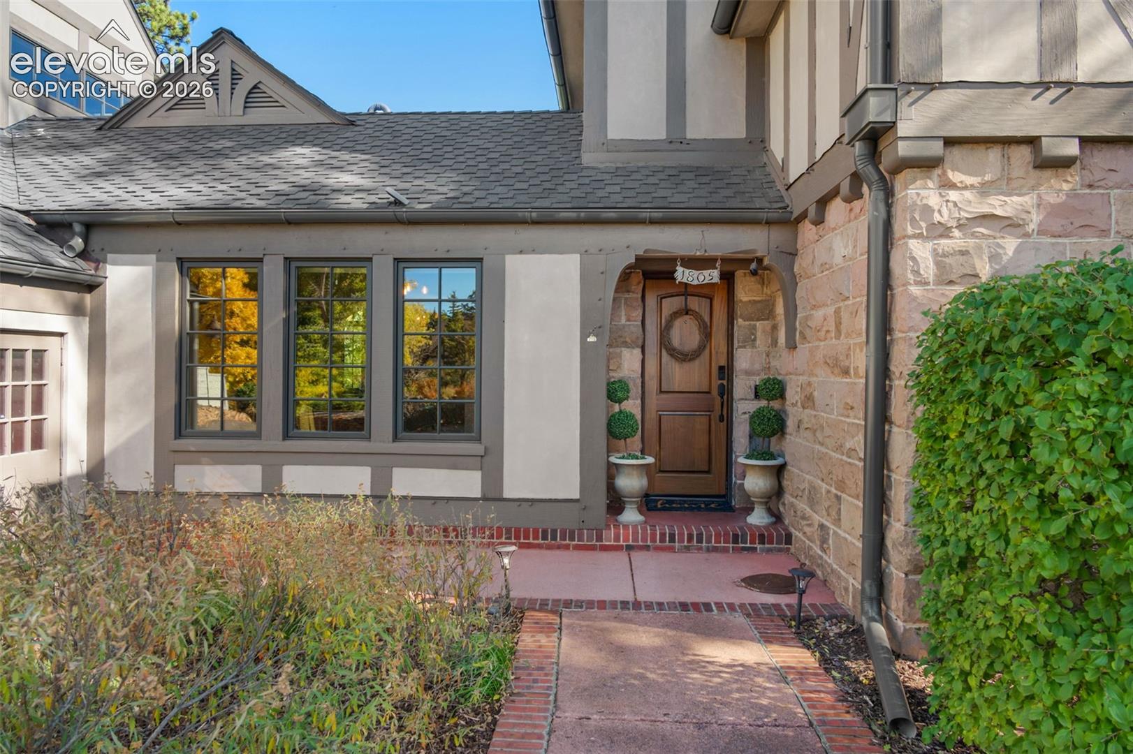 Tudor-style exterior featuring half-timbered detailing, stone masonry, a wood-paneled front door, and a brick paver walkway