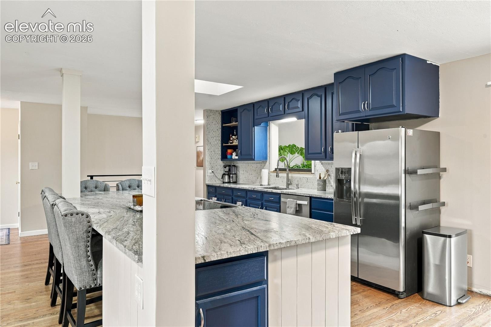 Kitchen featuring blue cabinetry, stone countertops, a stainless steel refrigerator, wood-finish flooring, and a large island with built-in seating area