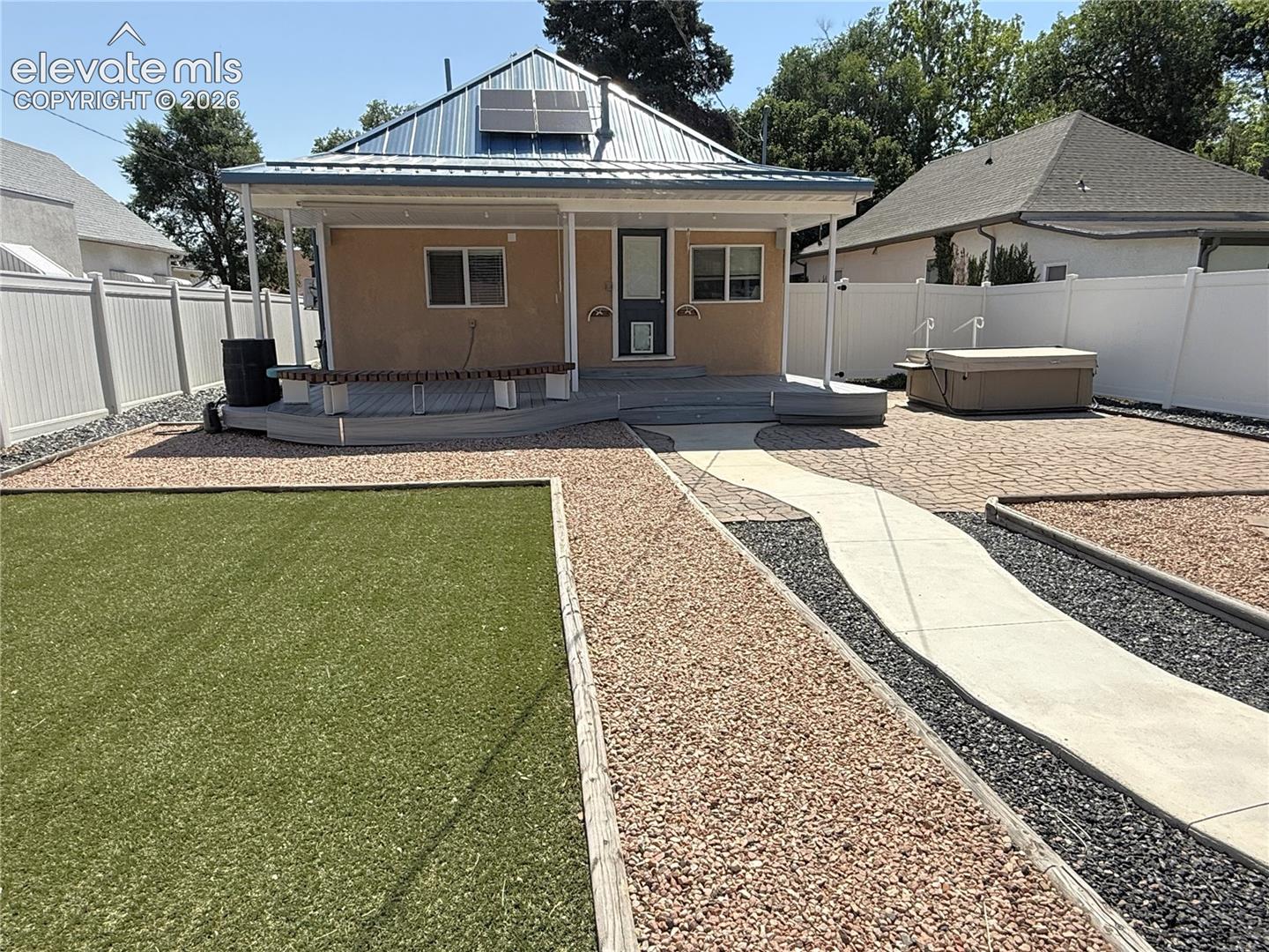 Backyard featuring a metal roof with solar panels, a composite deck with built-in seating, synthetic turf, a concrete walkway, and white vinyl privacy fencing