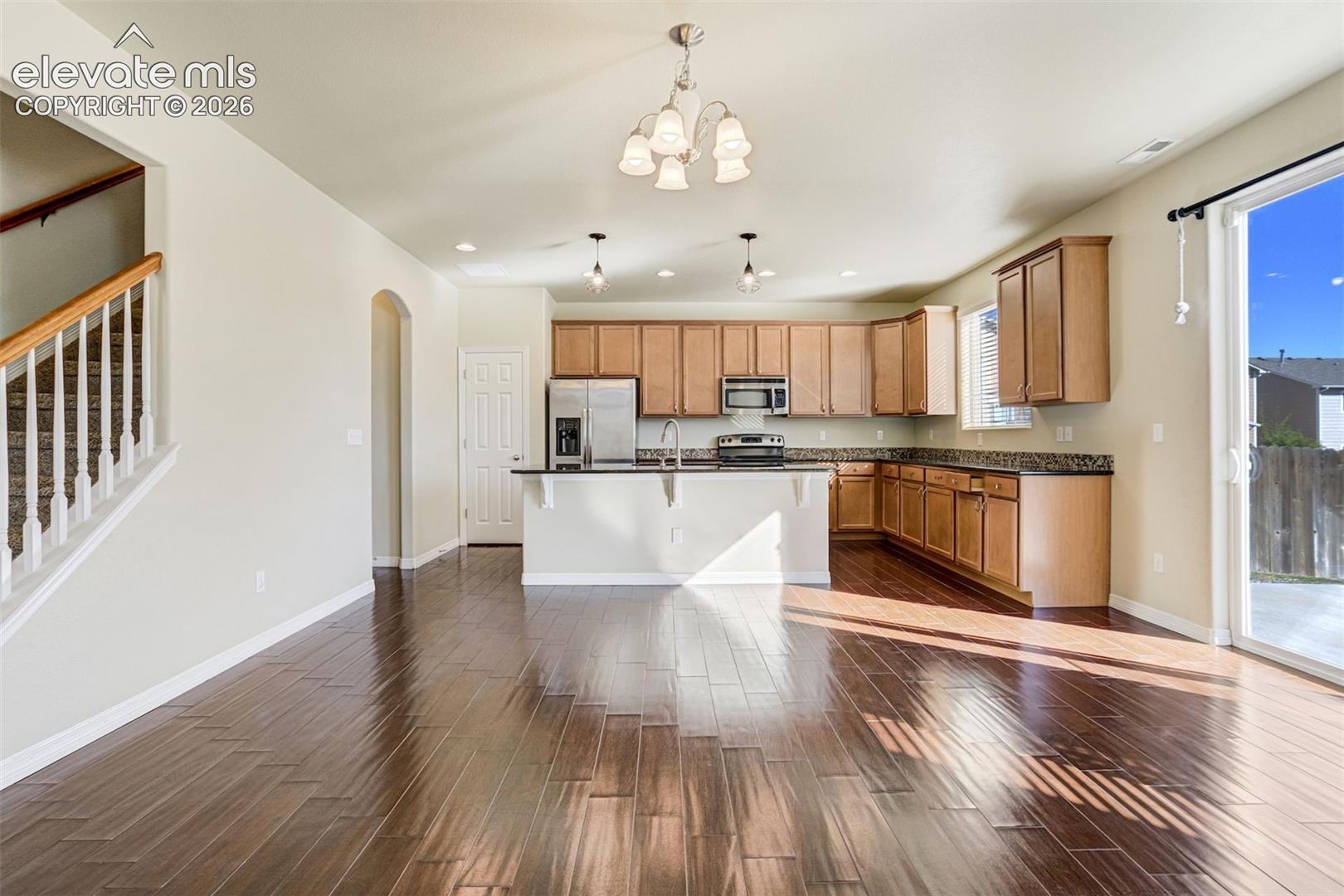 Open concept living area featuring dark wood-finish flooring, a kitchen with wood cabinetry and dark countertops, stainless steel appliances, and a sliding glass door to the exterior