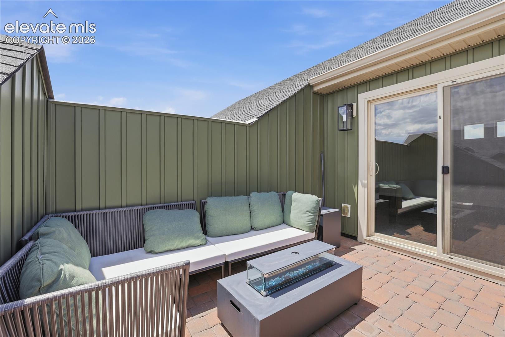 Private rooftop patio featuring a built-in fire pit, privacy wall, outdoor wall sconce, and sliding glass door access