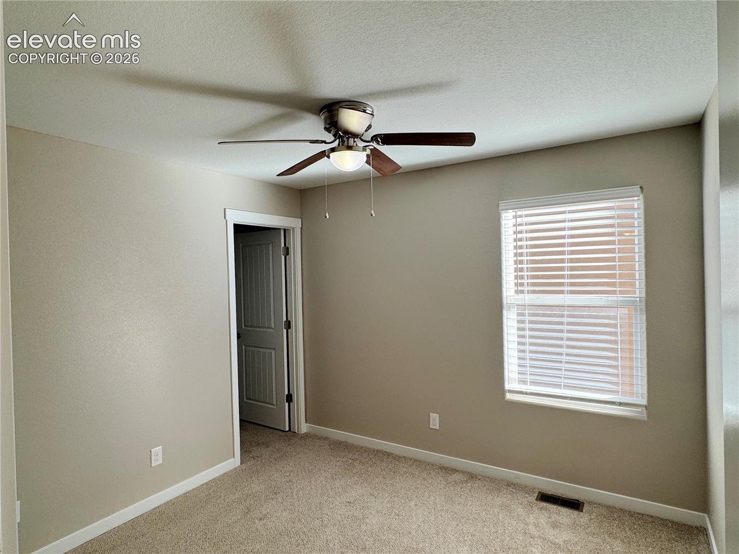 Interior room featuring carpeted flooring, a ceiling fan with integrated lighting, a multi-panel interior door, and a single-hung window with horizontal blinds