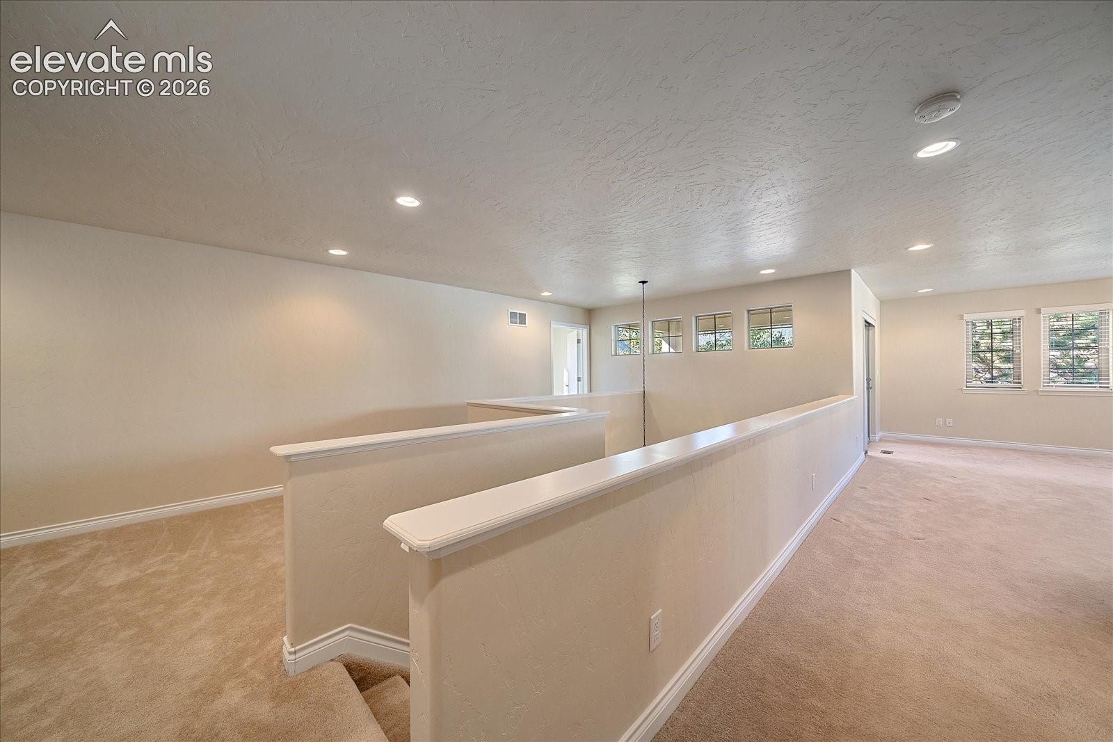 Open interior space featuring neutral carpeting, recessed lighting, grid-pattern windows, and a partial wall with a flat cap molding