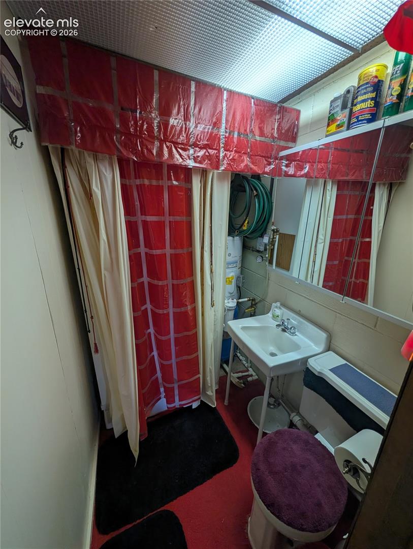 Compact bathroom featuring a white wall-mounted sink, toilet, and red flooring