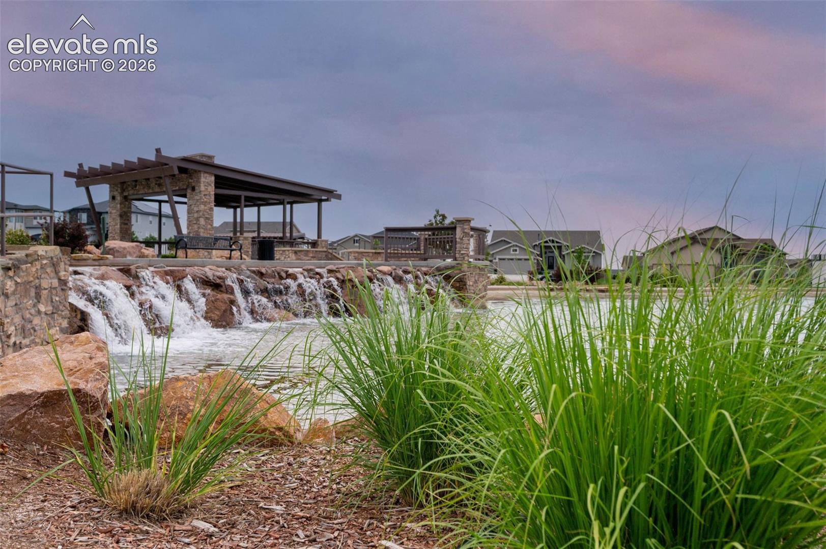 Stone-tiered water feature with a built-in pergola, stacked stone columns, and ornamental grasses