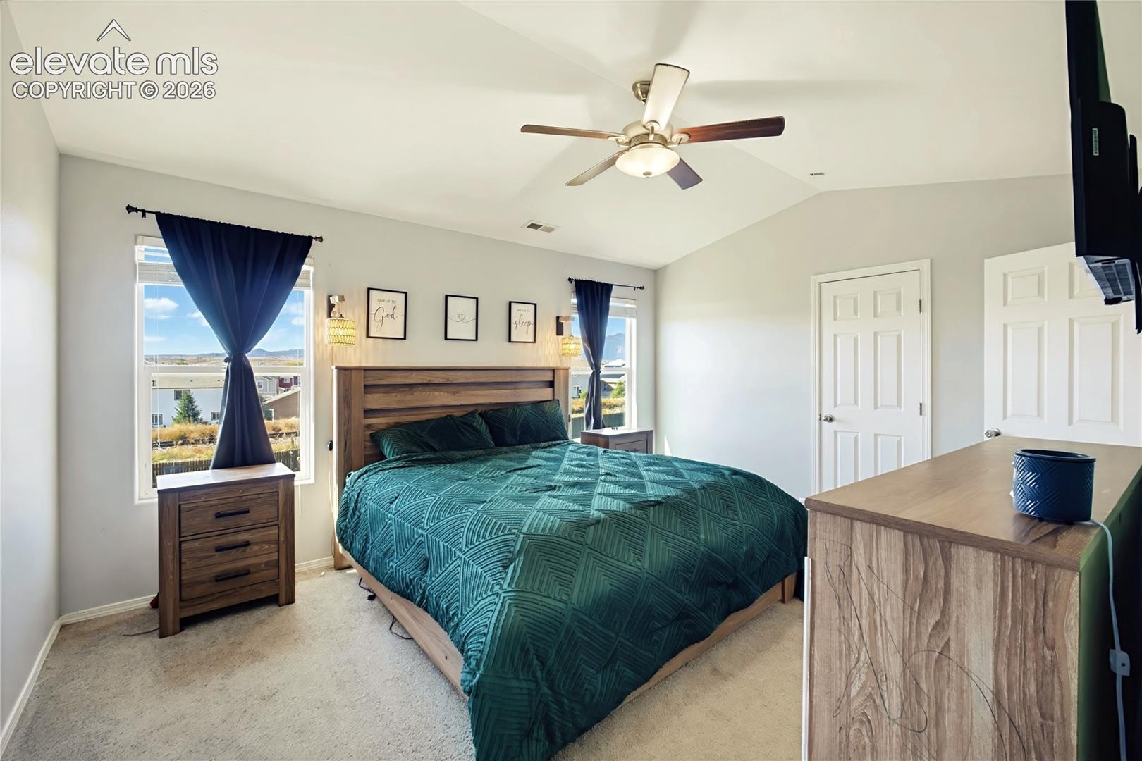 Vaulted ceiling with a ceiling fan, dual windows, and light gray wall paint