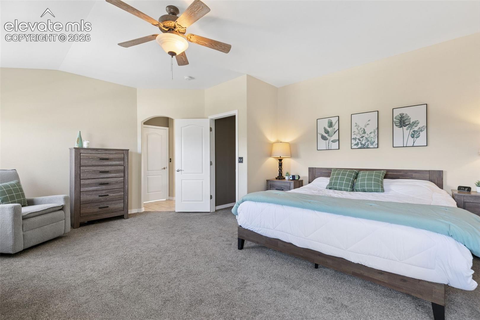 Neutral wall color, ceiling fan with integrated lighting, arched doorway, and gray carpeting