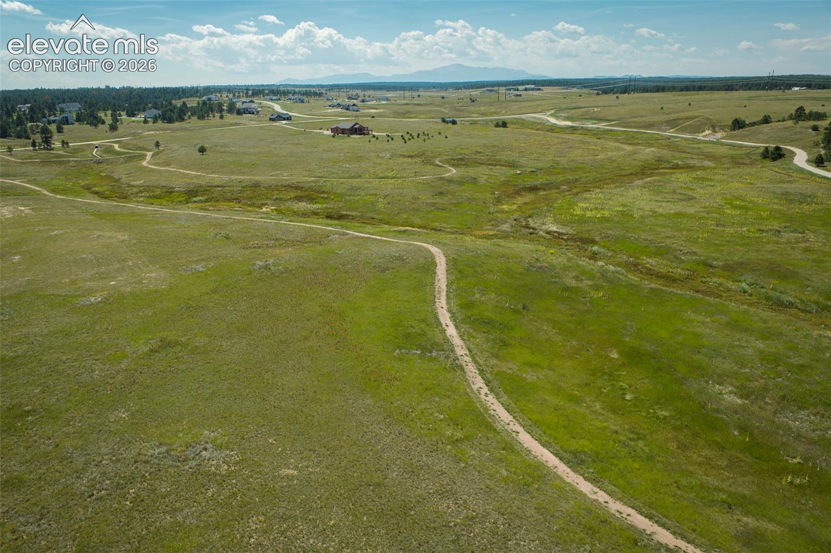 Expansive open terrain with natural grass, scattered trees, and distant residential structures