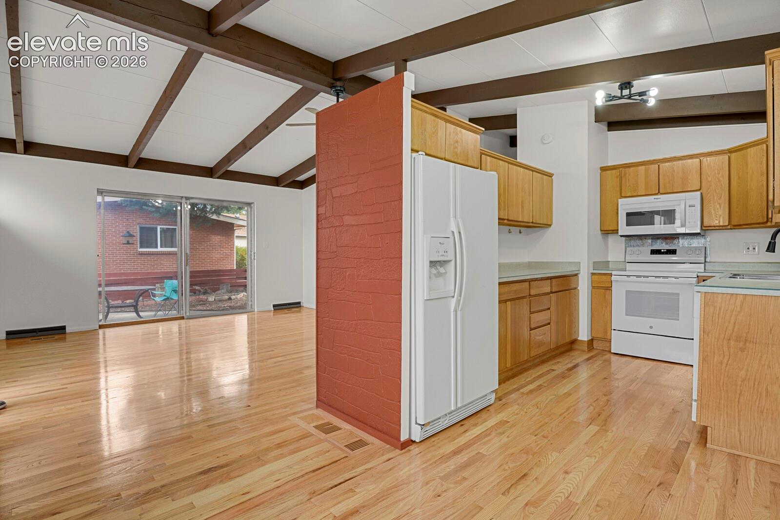 Vaulted ceiling with exposed wood beams, wood-finish flooring, masonry accent wall, and cabinetry with New range/oven, microwave and integrated appliances