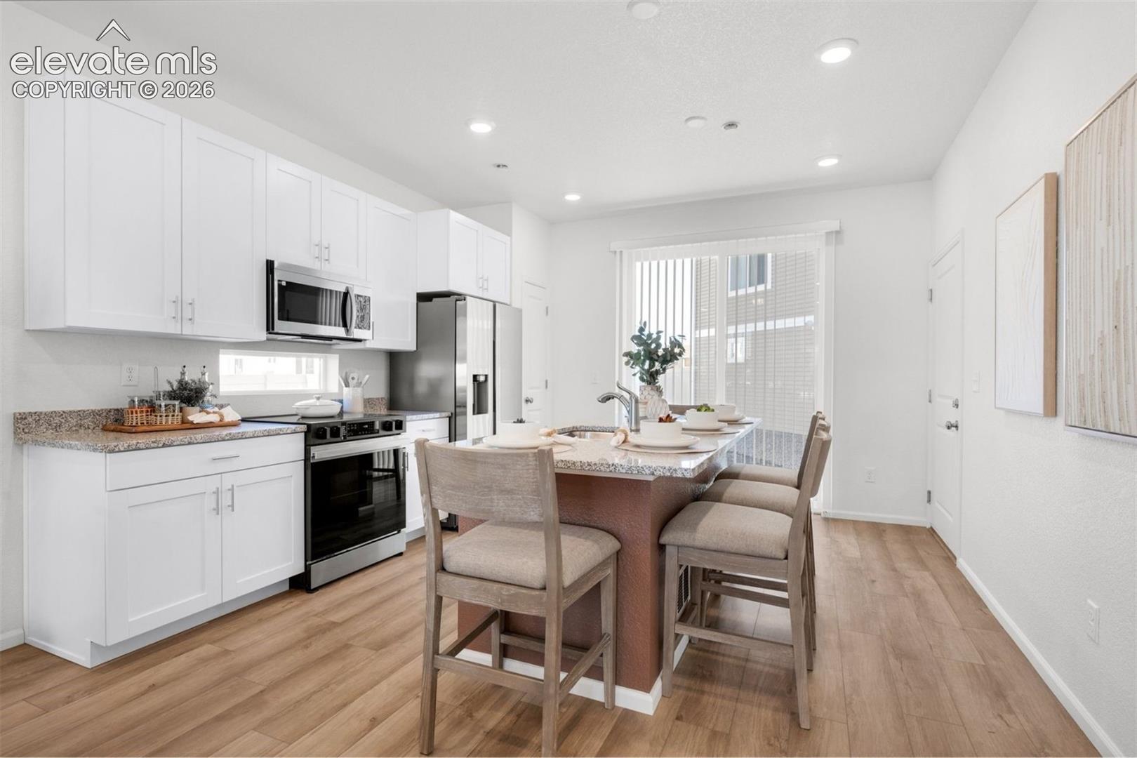 Kitchen featuring wood-finish flooring, white cabinetry, stainless steel appliances, and a central island with a stone countertop
*photos of a model home*