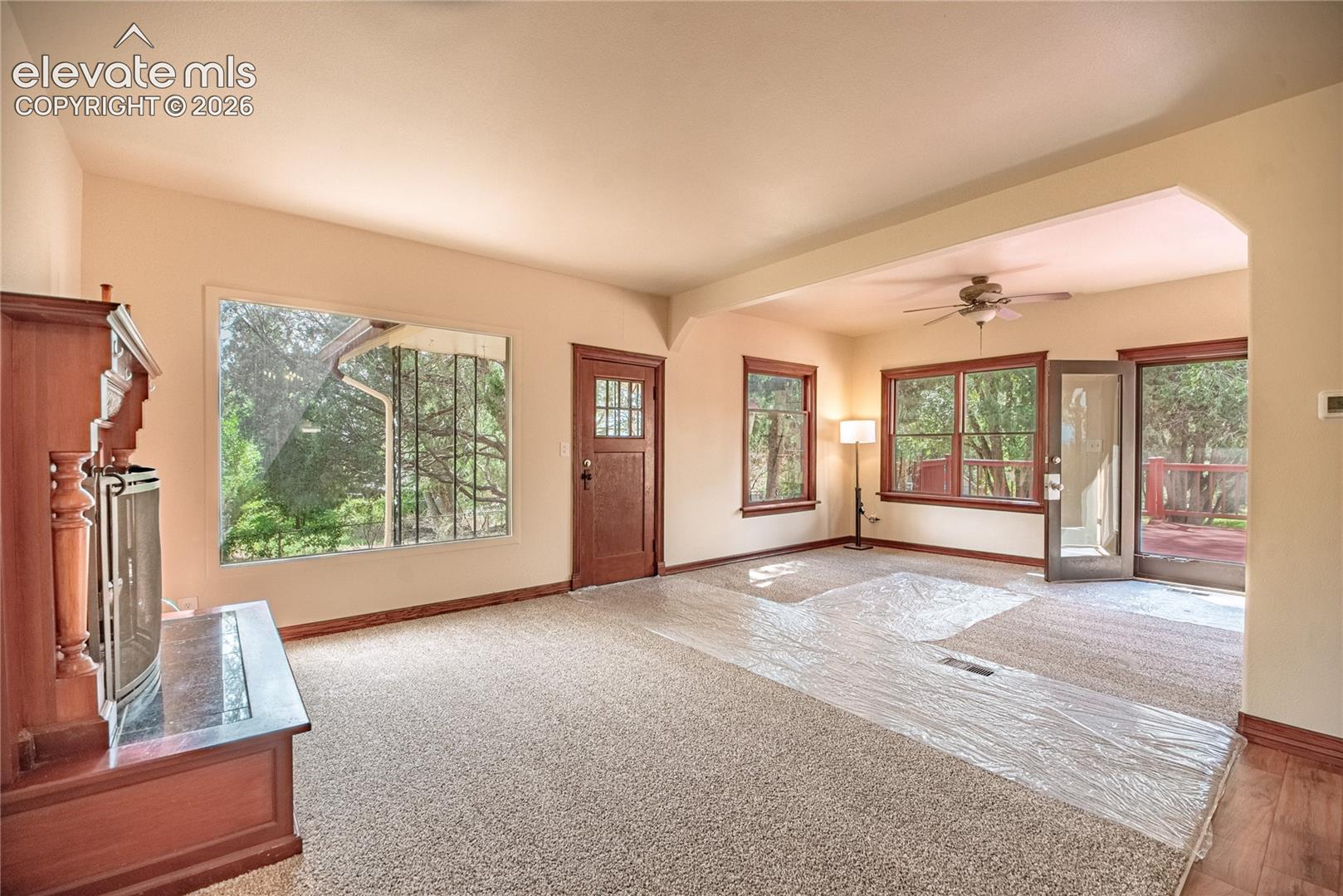 Arched entryway, rich wood-frame windows, ceiling fan, wood-finish flooring, and a fireplace with a stone-finish hearth