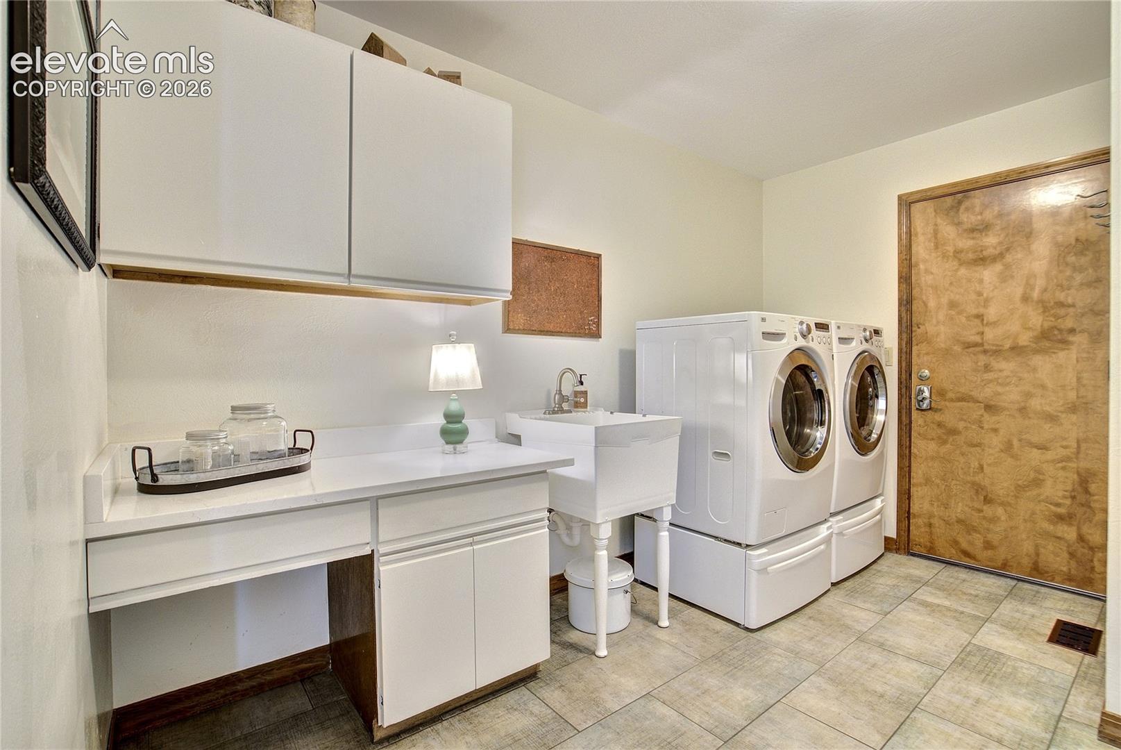 A generous laundry room offers abundant cabinetry, utility sink + a versatile folding counter/desk.