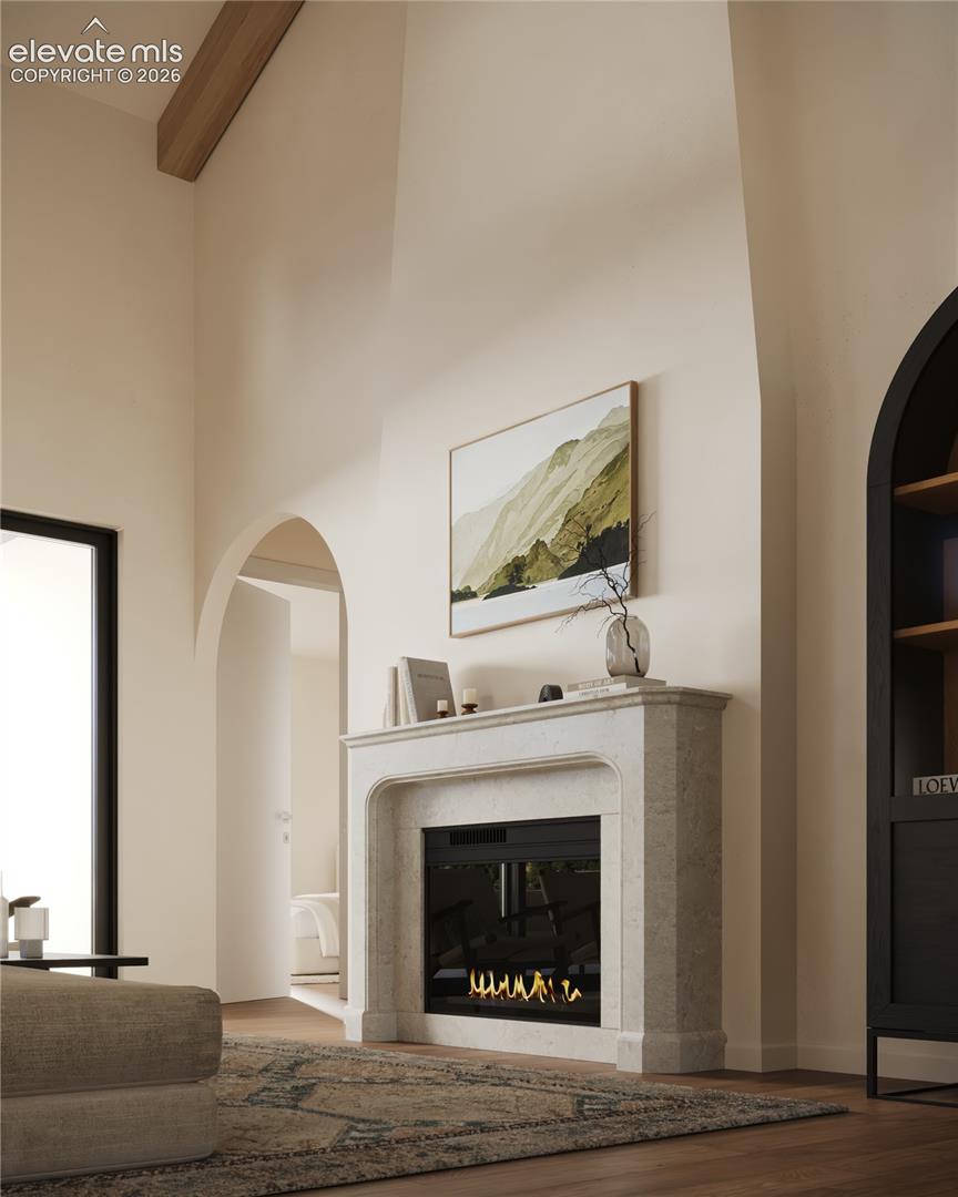 Vaulted ceiling with exposed wood beam, elegant fireplace with stone surround, wood-finish flooring, and arched doorway