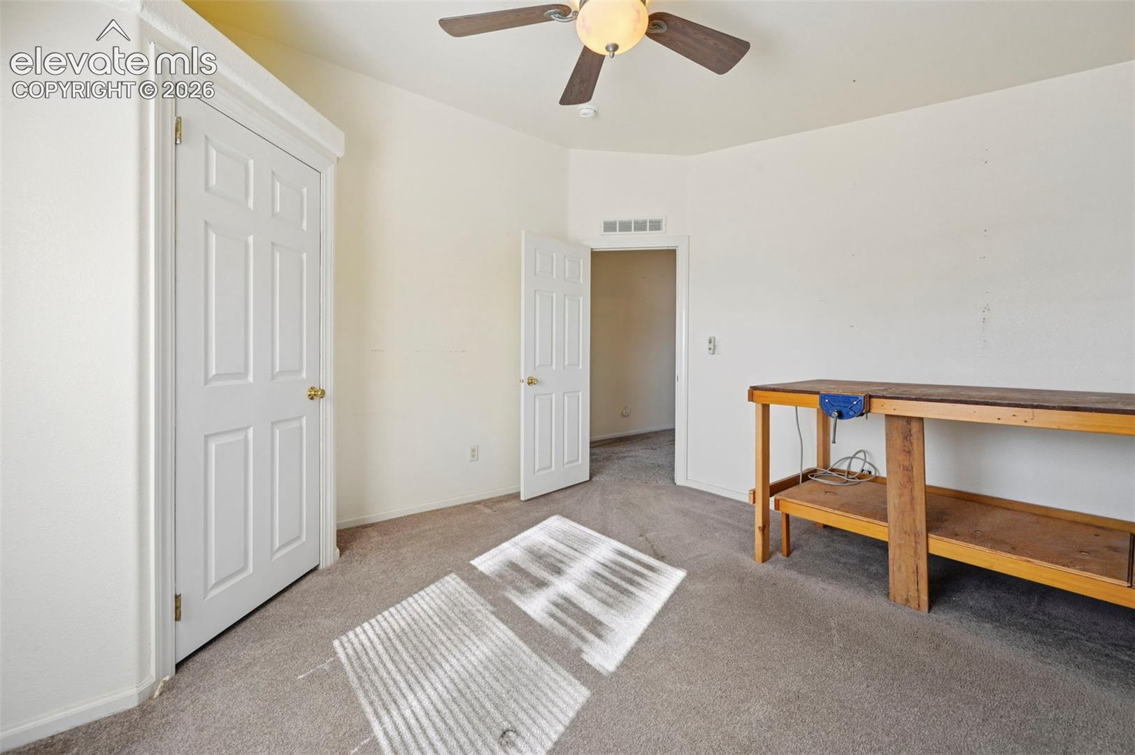 Neutral-toned interior space featuring wall-to-wall carpeting, a ceiling-mounted light fixture with fan, and white panel doors