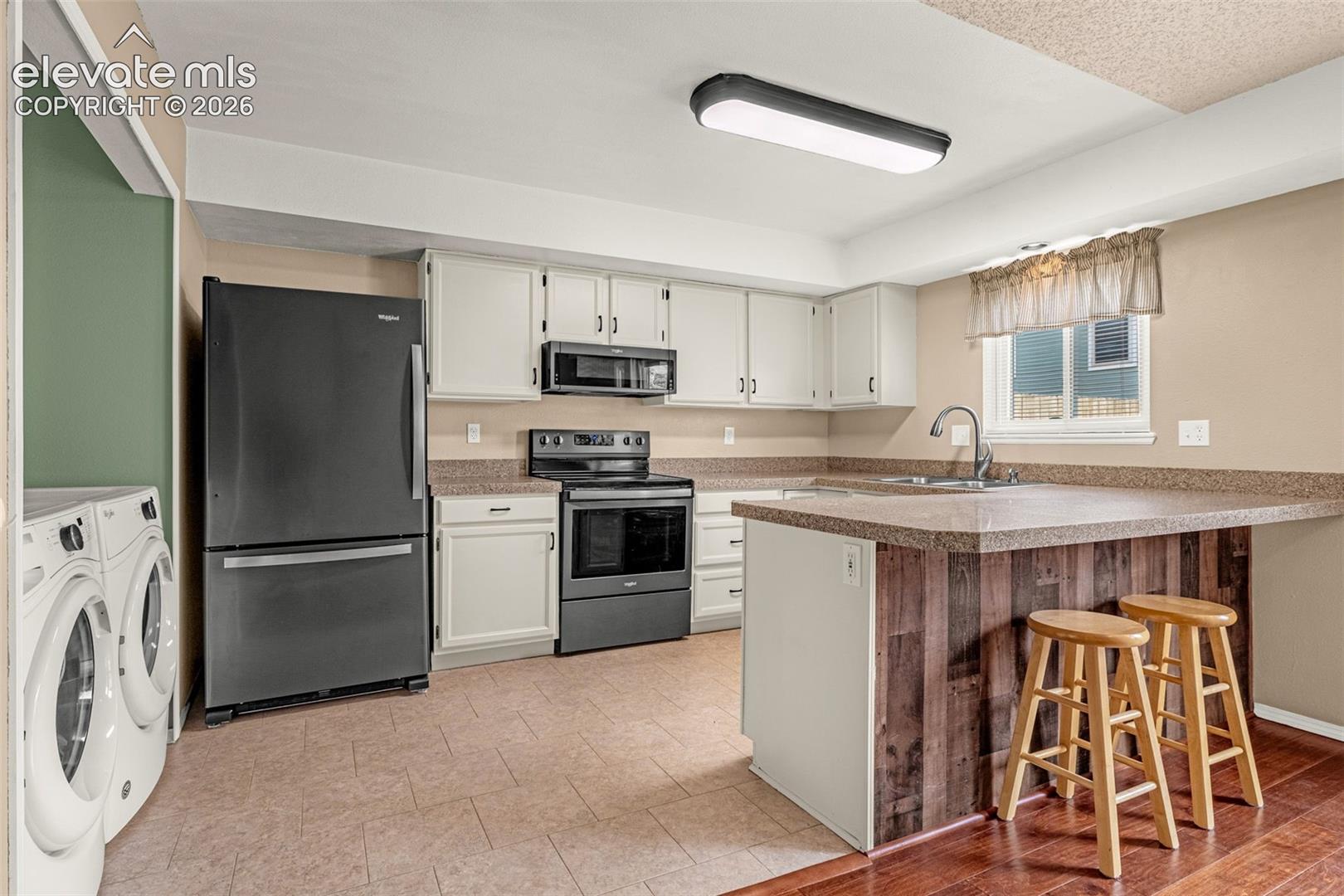 Kitchen featuring white cabinetry, dark stainless steel appliances, a breakfast bar with wood-finish paneling, and a stainless steel sink with a gooseneck faucet