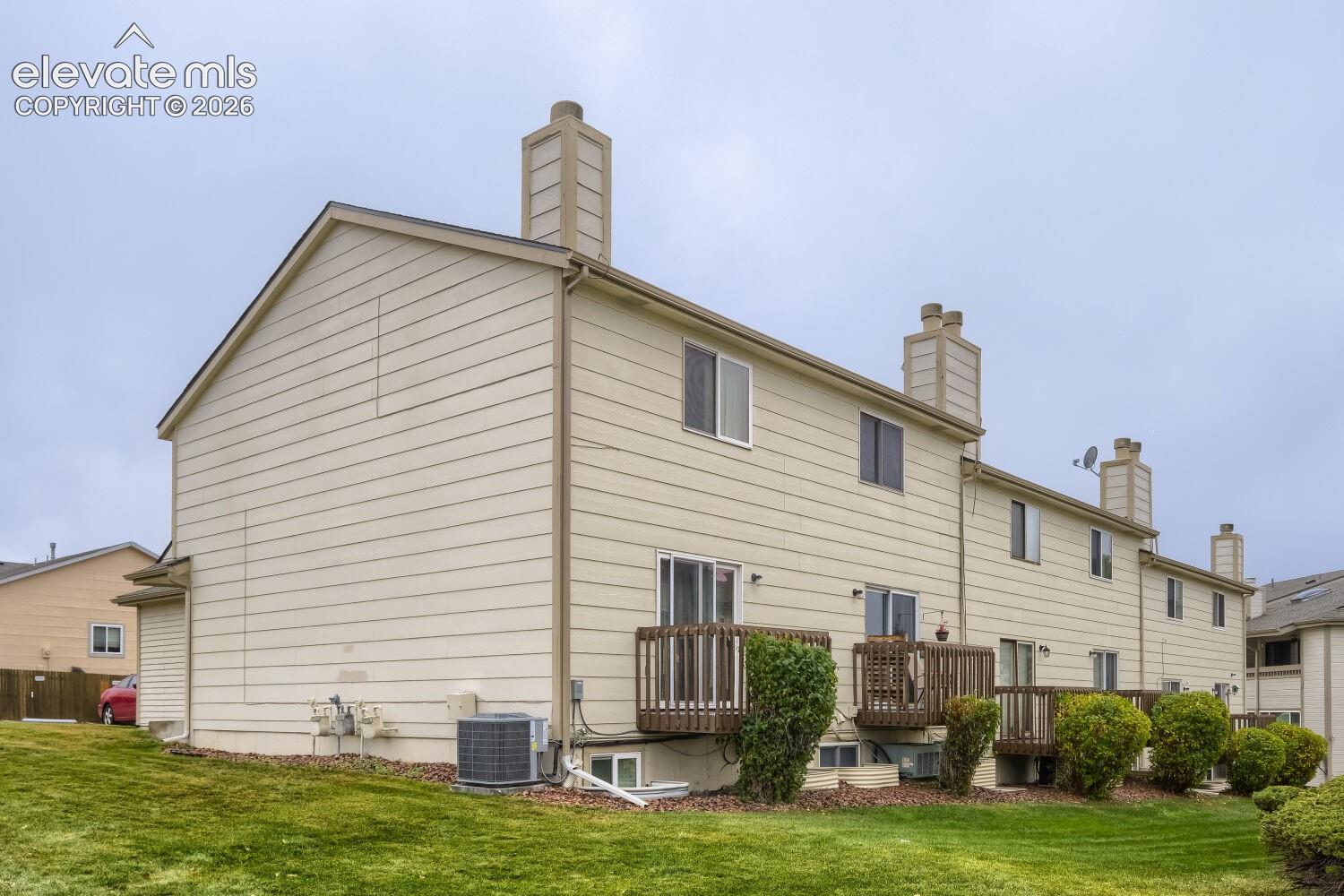 Exterior elevation featuring beige horizontal siding, multiple chimneys, raised wooden decks, and sliding glass door access