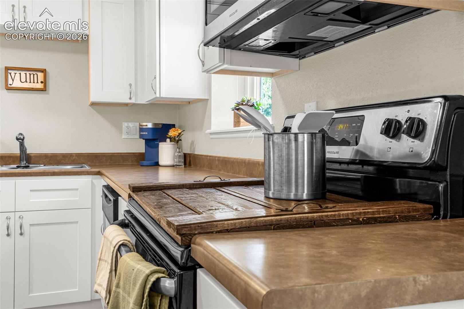 Kitchen featuring white shaker-style cabinetry, solid-surface countertops, and stainless steel appliances including an over-the-range microwave