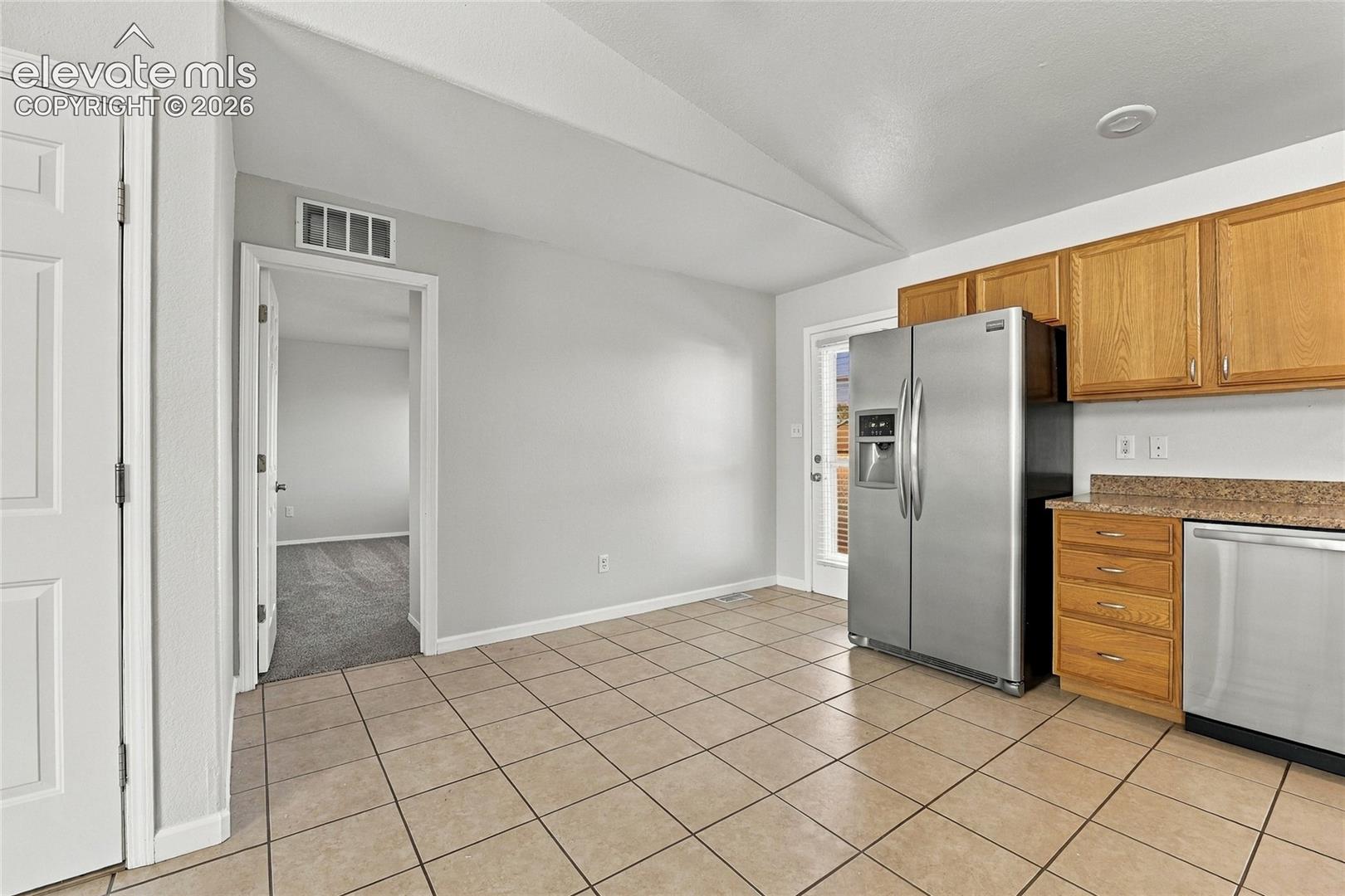Kitchen featuring light wood-finish cabinetry, stone-texture countertops, stainless steel appliances, and ceramic tile flooring