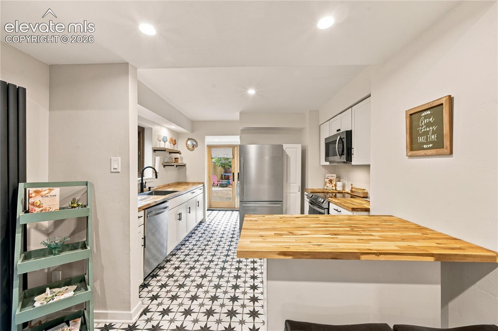 Kitchen featuring wood-finish butcher block countertops, stainless steel appliances, white cabinetry, and geometric patterned tile flooring