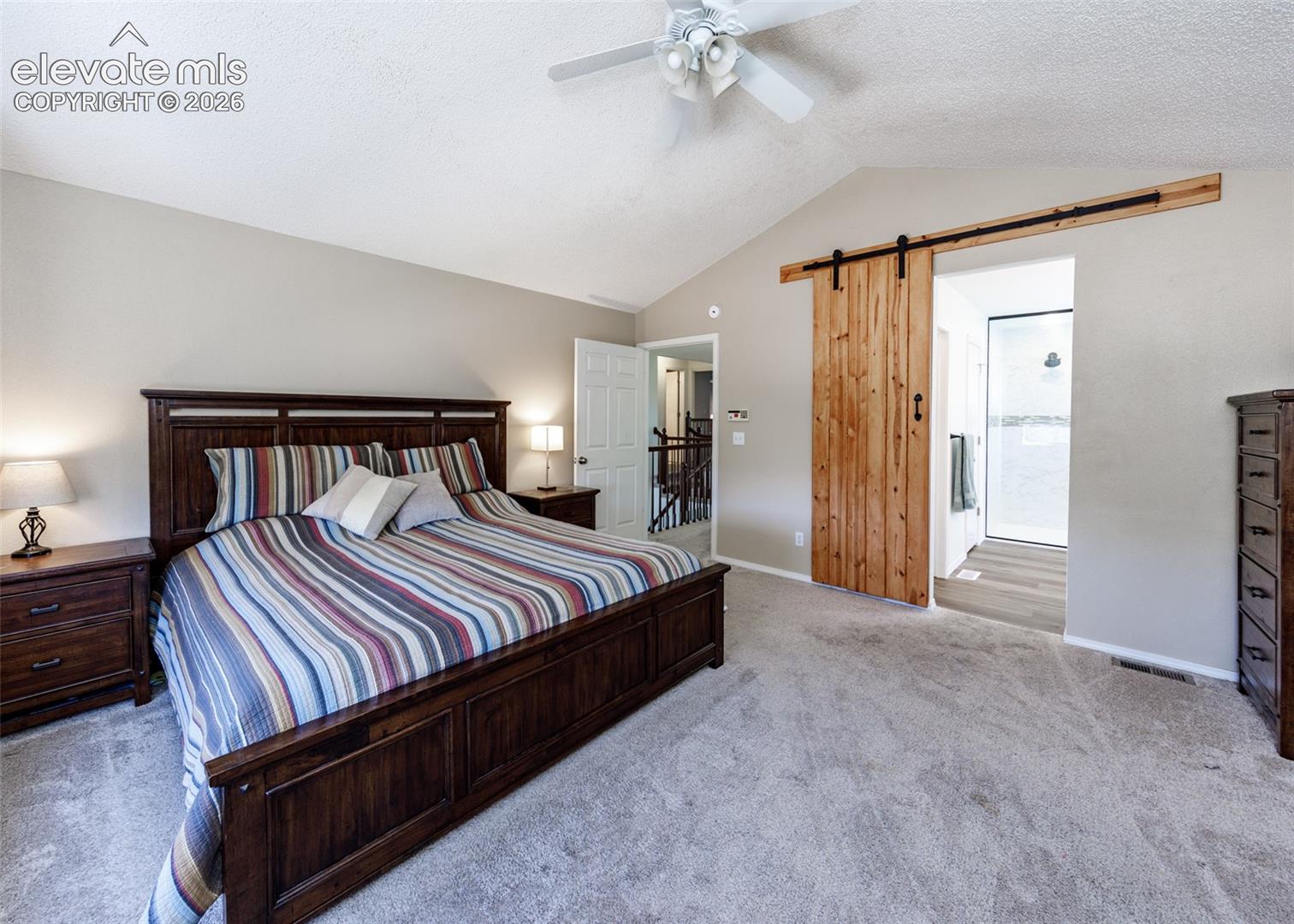 Vaulted ceiling with a ceiling fan, light-toned wall paint, natural wood-finish barn door, and carpet flooring
