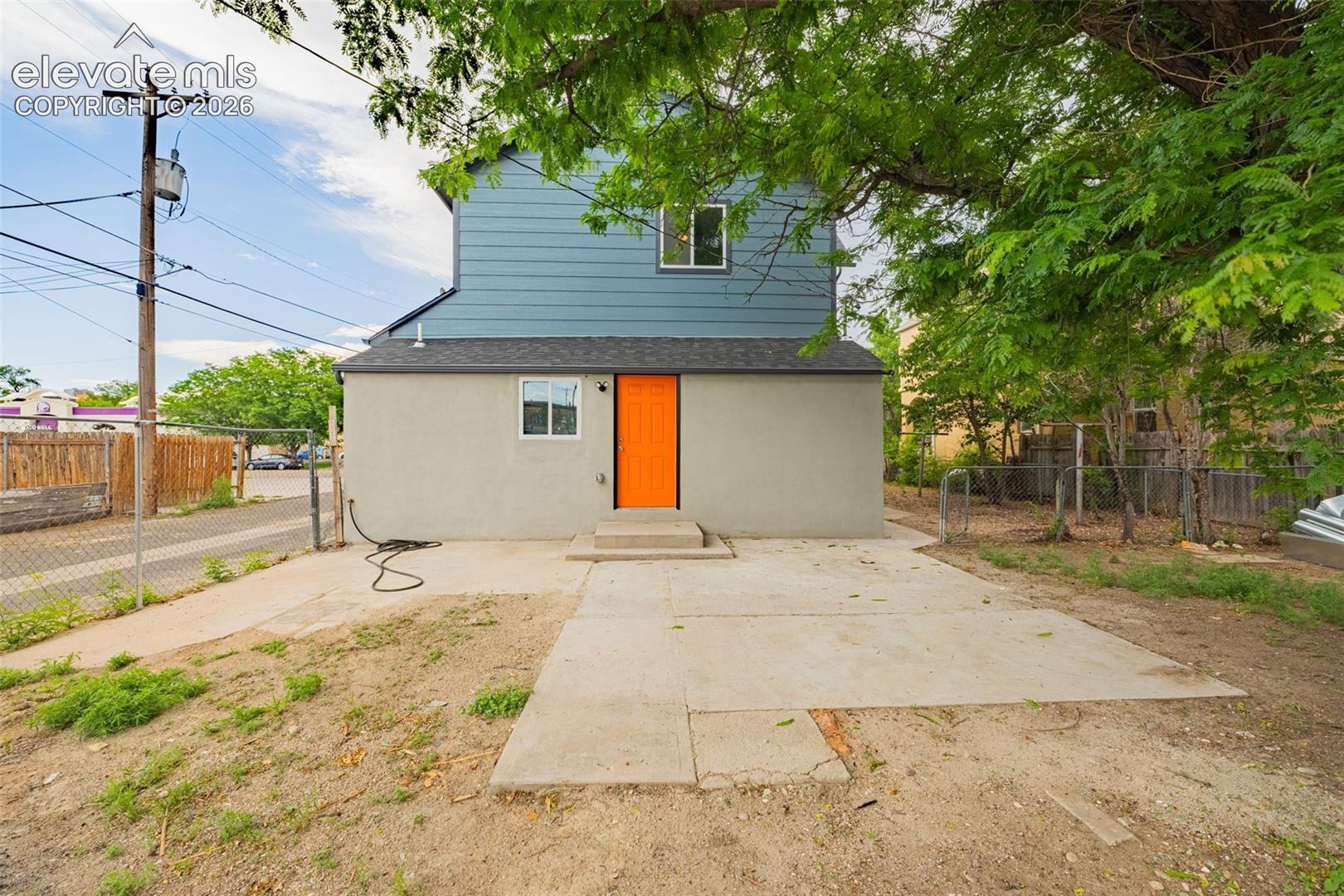 Rear exterior featuring a vibrant orange door, light gray stucco, and blue horizontal siding