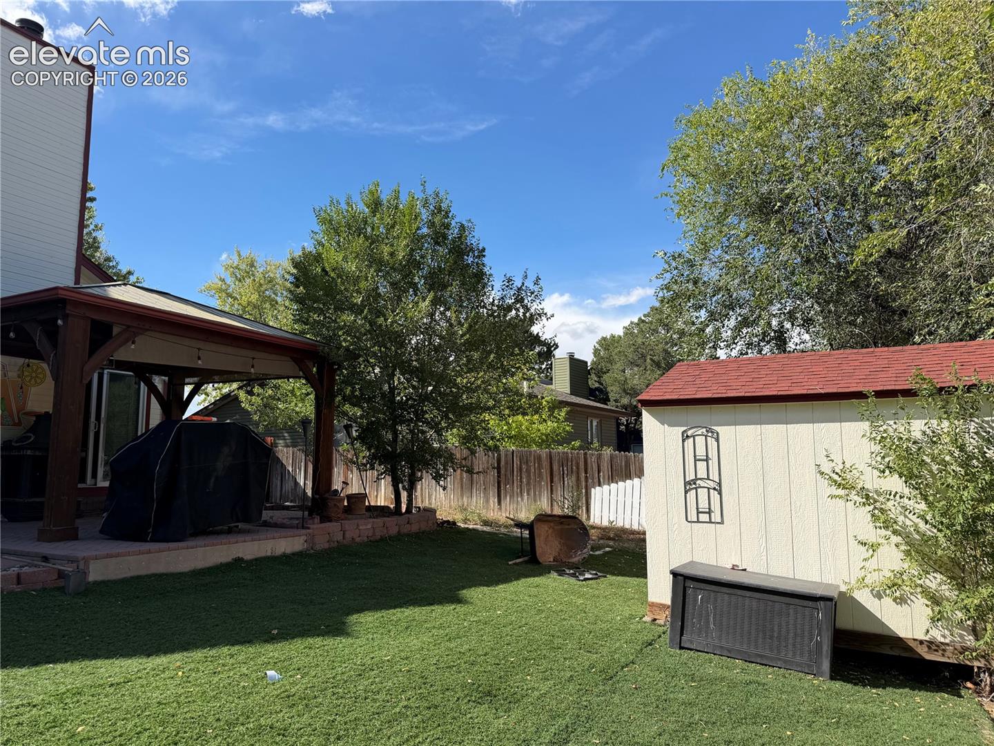Expansive backyard featuring a covered patio with string lighting, a manicured lawn, and a storage shed with a red roof