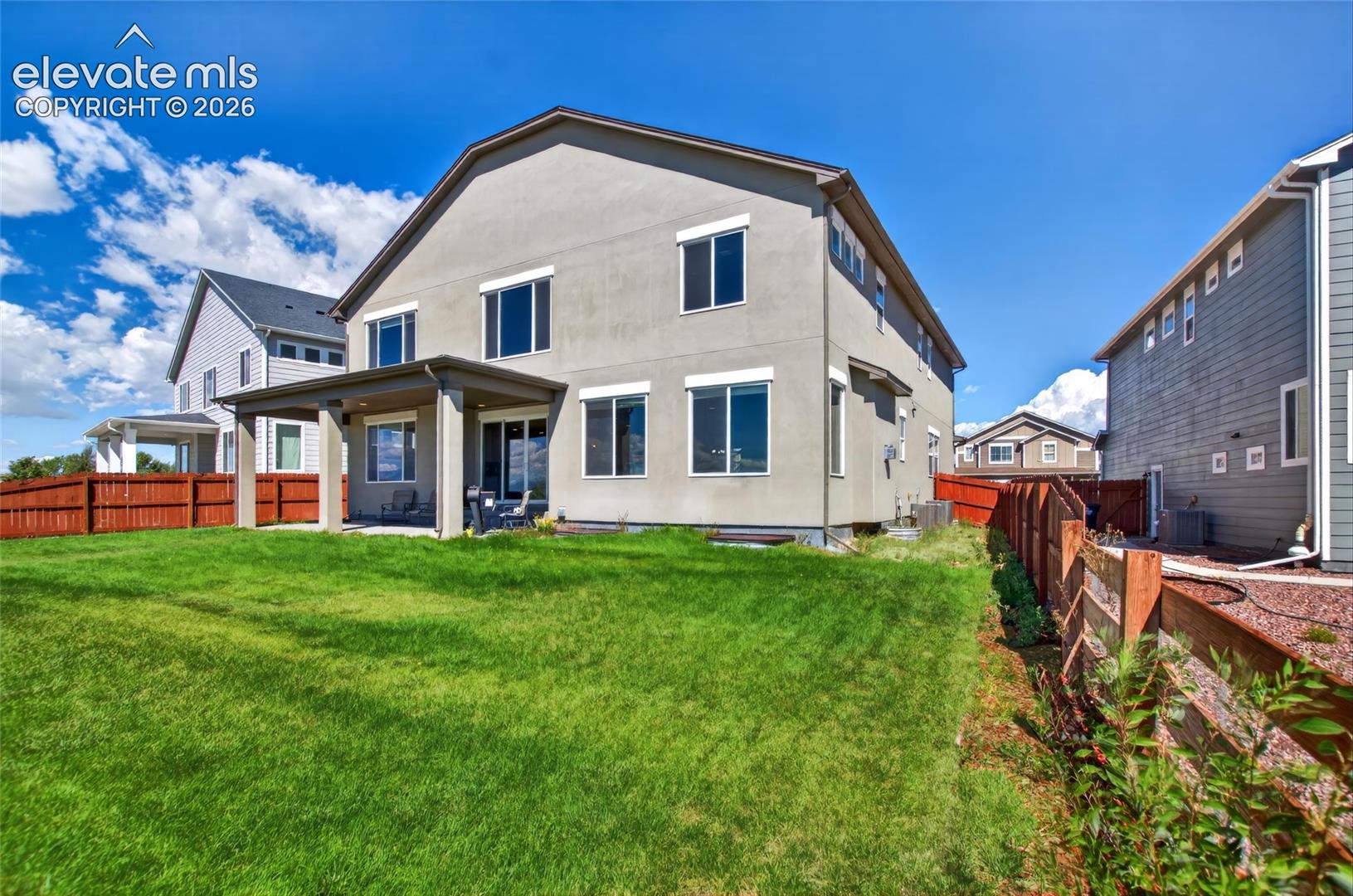 Expansive green lawn, covered patio, stucco exterior, privacy fencing, and multiple windows