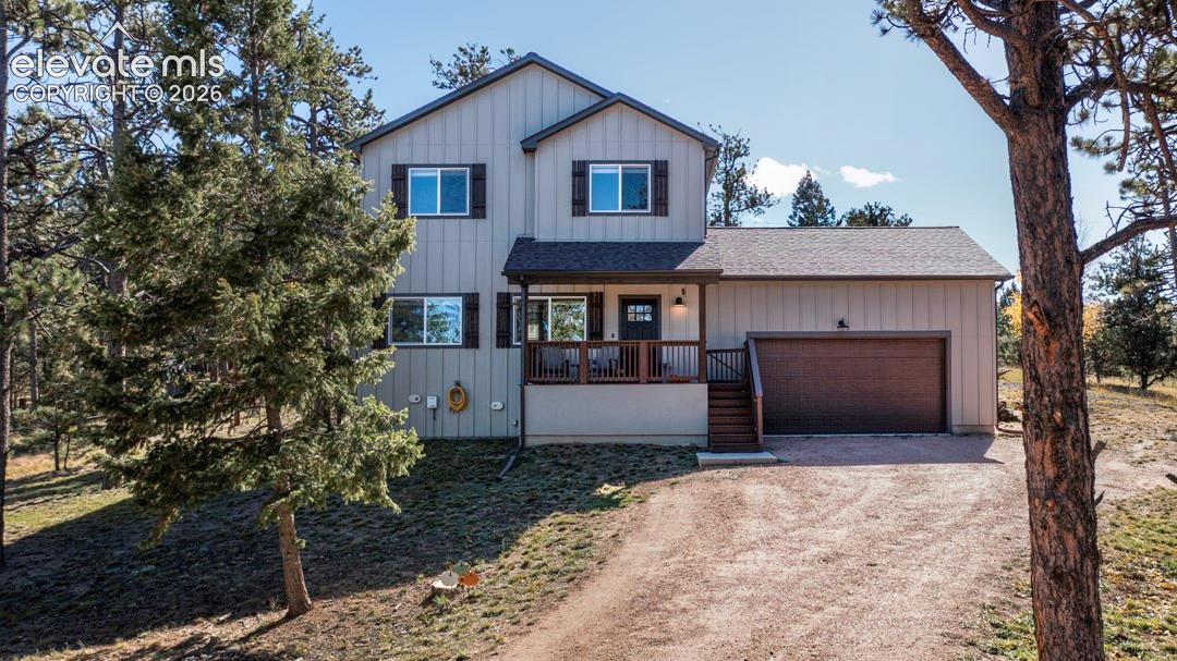 Two-story exterior featuring vertical siding, decorative shutters, a covered front porch with a wood railing, and an attached garage