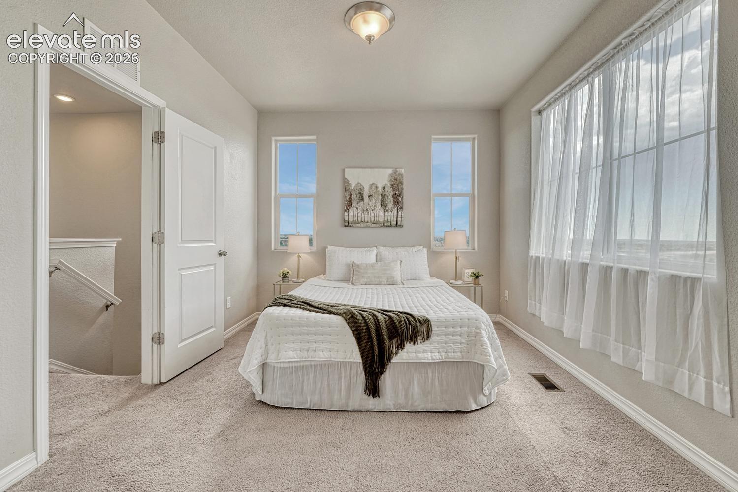 Upper level Primary Bedroom with wall of windows, neutral carpet, adjoining bathroom and walk in closet.