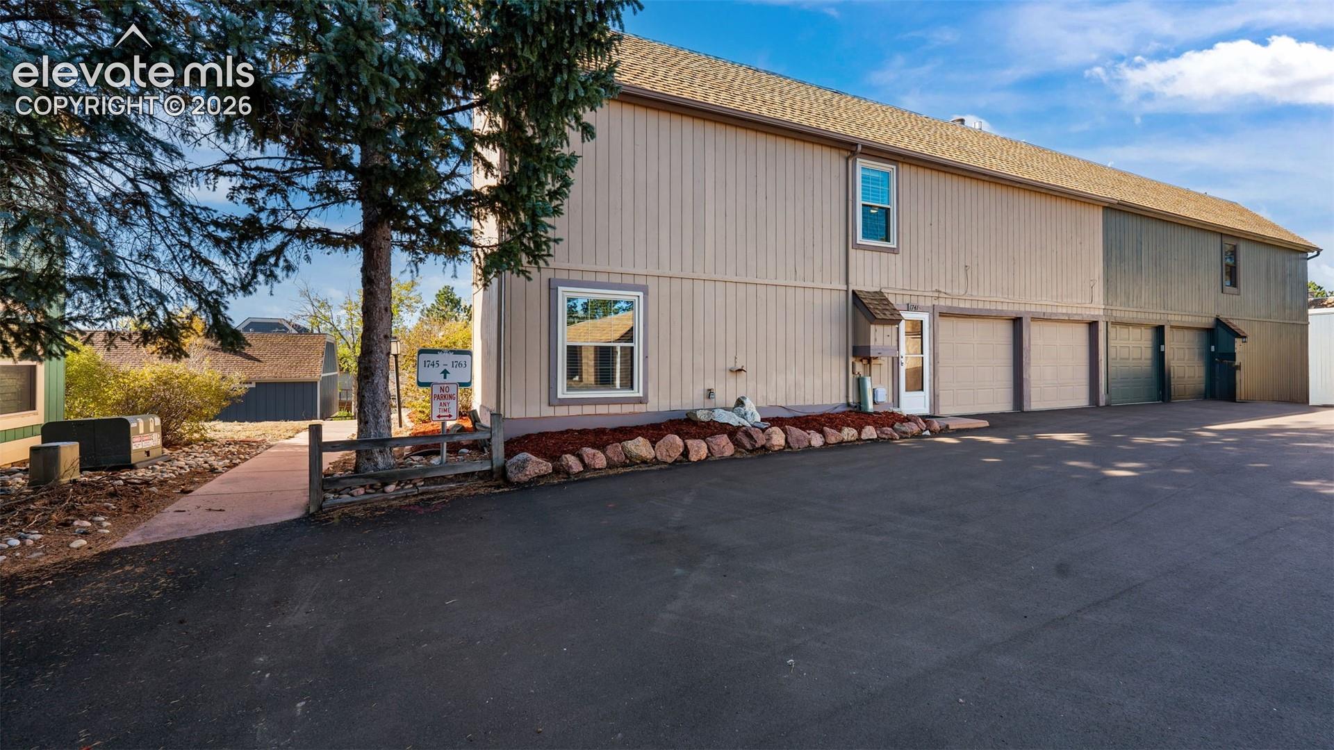 Multi-unit structure with vertical board-and-batten siding, asphalt shingle roofing, multiple attached garage bays, and paved exterior parking area