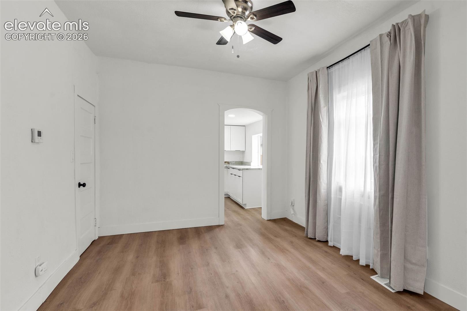 Interior space featuring wood-finish flooring, a ceiling-mounted light fixture with a three-blade fan, and an arched doorway