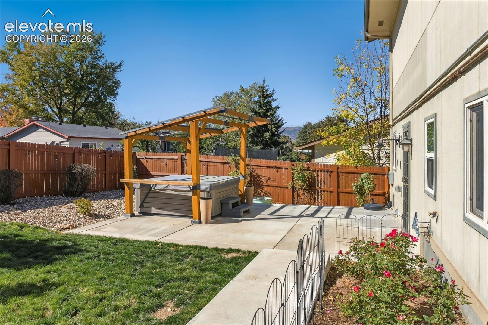 Backyard featuring a concrete patio, wood-frame pergola, integrated hot tub, privacy fencing, and a manicured lawn