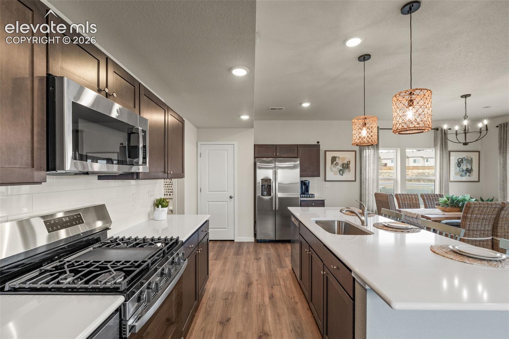 Kitchen featuring stainless steel appliances, dark wood-finish cabinetry, white subway tile backsplash, and light-toned countertops