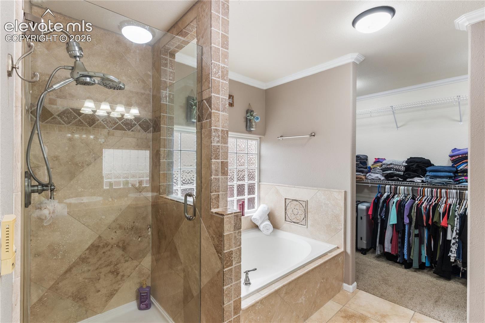 Walk-in shower with stone tile surround, glass enclosure, and dual-head fixture; built-in soaking tub featuring stone tile deck; glass block window