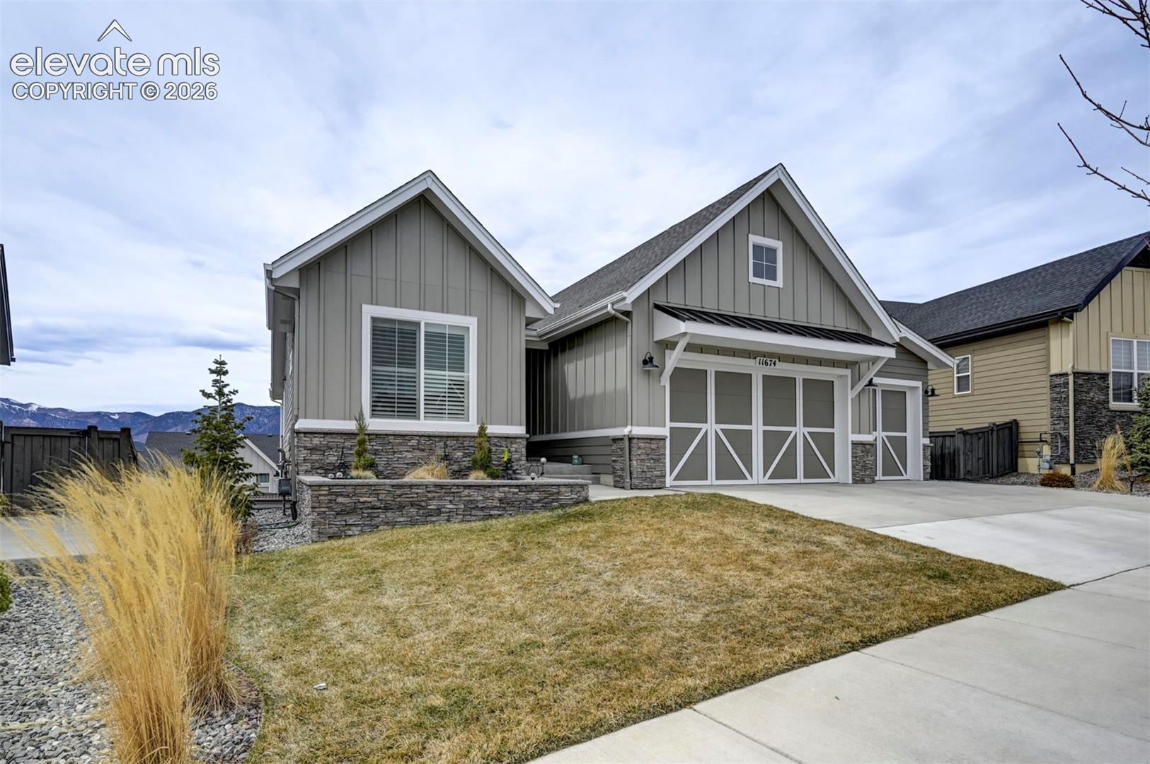 Gable roofline, vertical panel siding, stone accent facade, two-car garage, and concrete driveway
