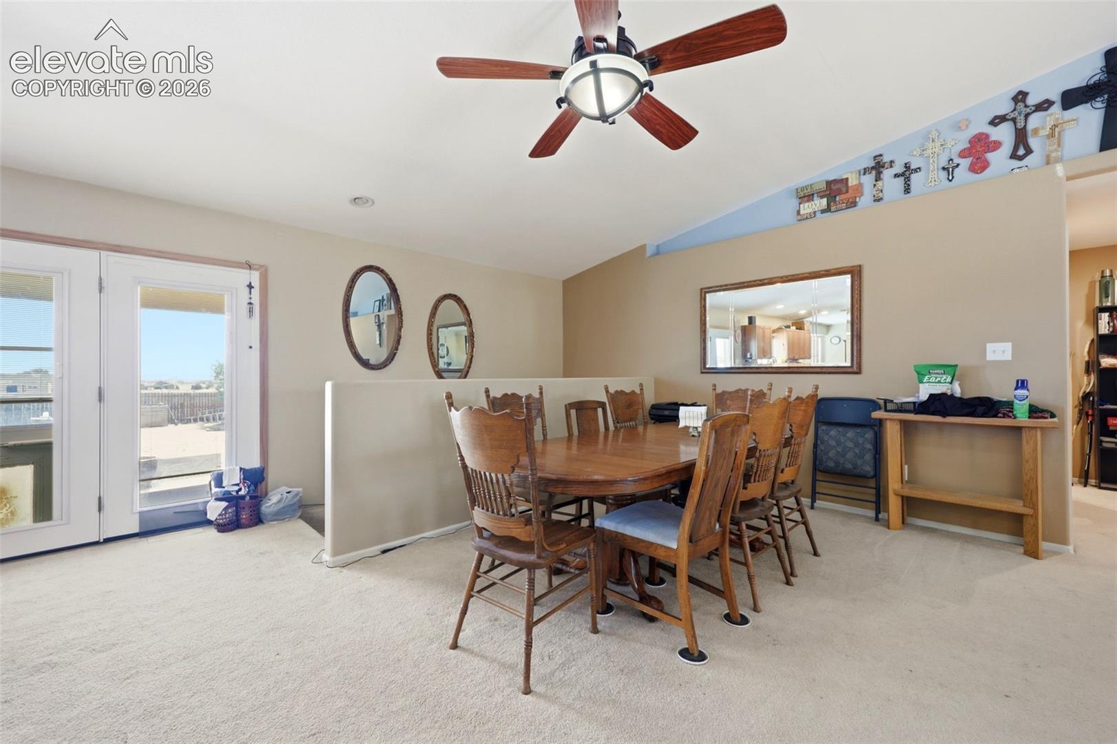 Carpeted interior space featuring a ceiling fan with integrated lighting, a partial wall, and a pair of French doors providing exterior access