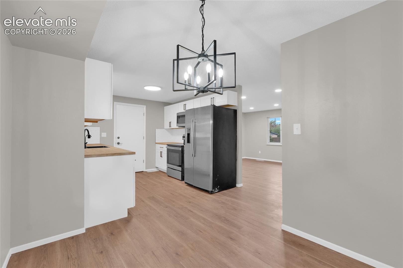 Kitchen featuring wood-finish flooring, white cabinetry, stainless steel appliances, and a modern chandelier