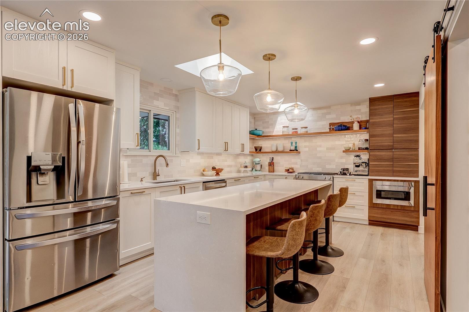 Modern kitchen featuring white shaker cabinetry, stainless steel appliances, a center island with counter seating, wood-finish flooring, and a barn door