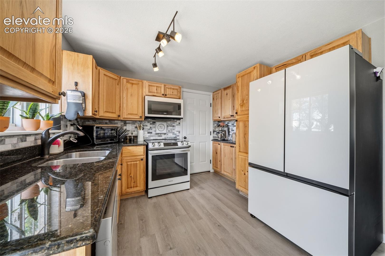 Full kitchen featuring wood cabinetry, stainless steel appliances, dark stone countertops, and a tile backsplash
