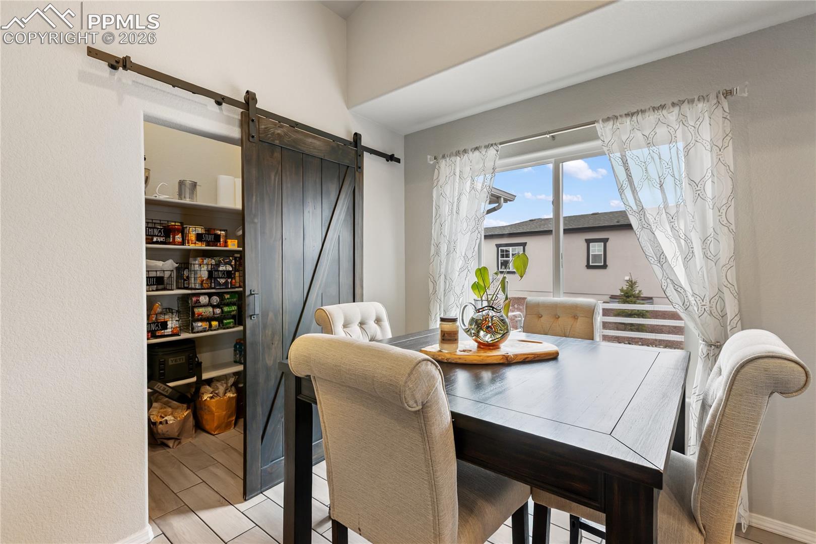Barn door pantry with extensive shelving, ceramic tile flooring, and natural light from a large window