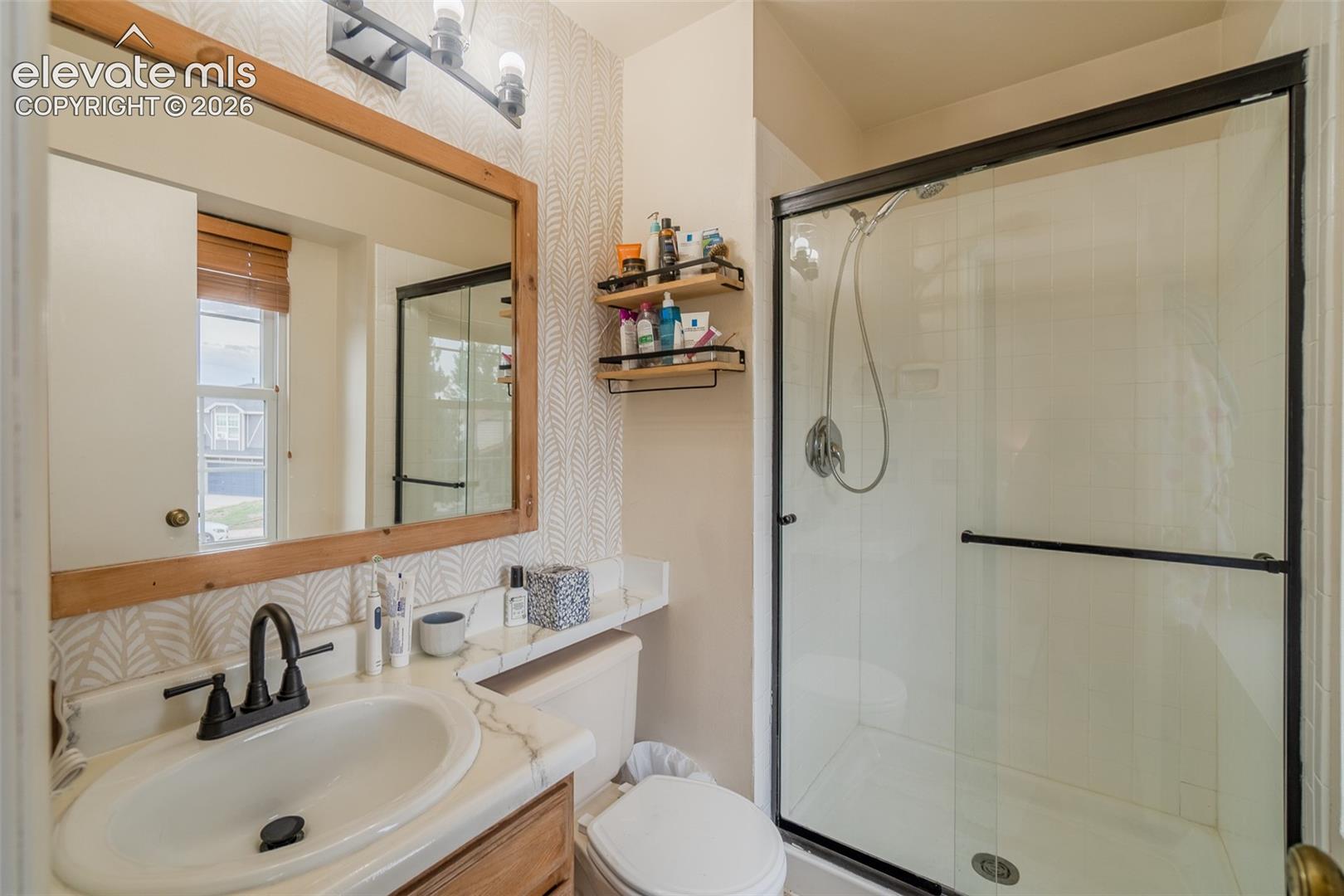Framed mirror with integrated lighting, single-basin vanity with a new sink, black faucet, and a glass-enclosed shower with black trim