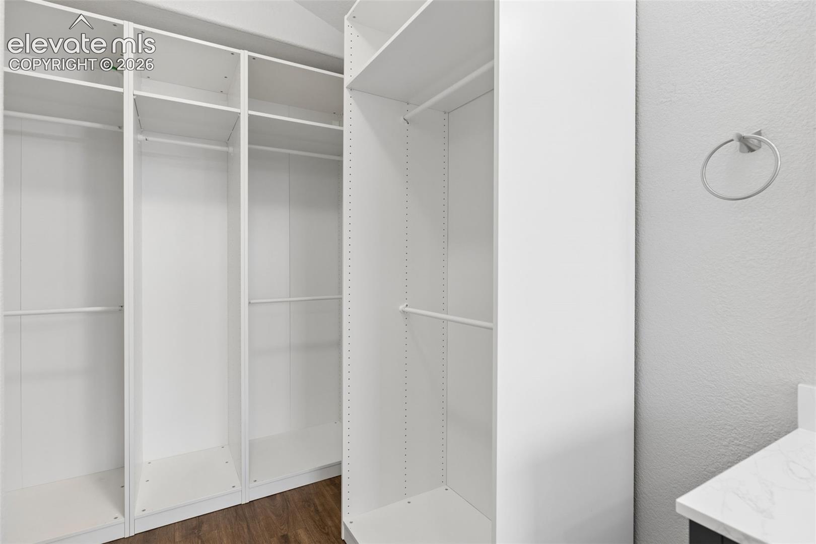 Custom white cabinetry with adjustable shelving and hanging rods, wood-finish flooring, and a circular wall-mounted towel ring