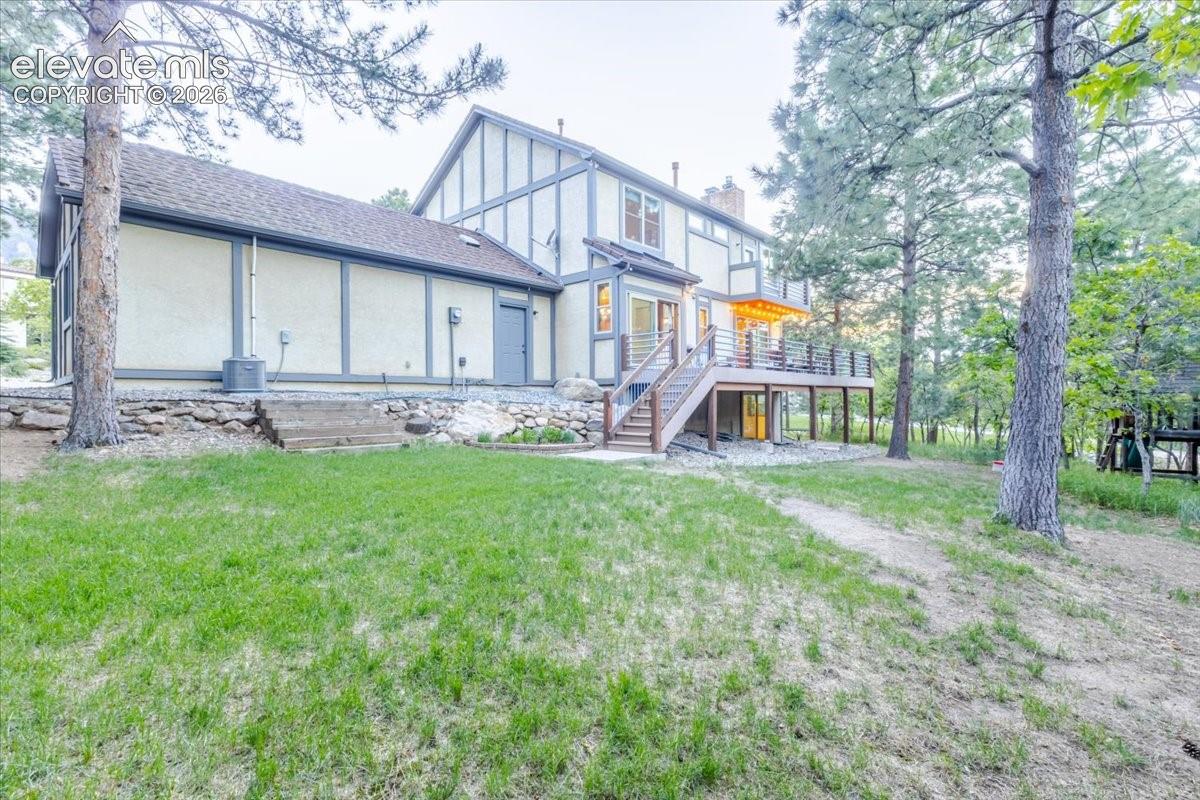 Expansive rear exterior featuring a multi-level deck with metal railings and built-in lighting, a stucco and wood-trim facade, and a stone retaining wall