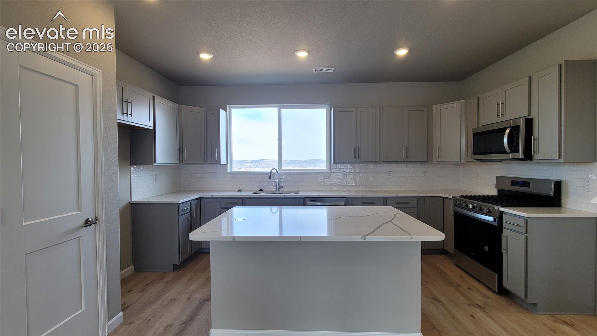 Grand Kitchen with Quartz countertops, pantry, plenty of cabinets, island providing additional seating, view from sink, stainless steel gas range, microwave, and dishwasher! 