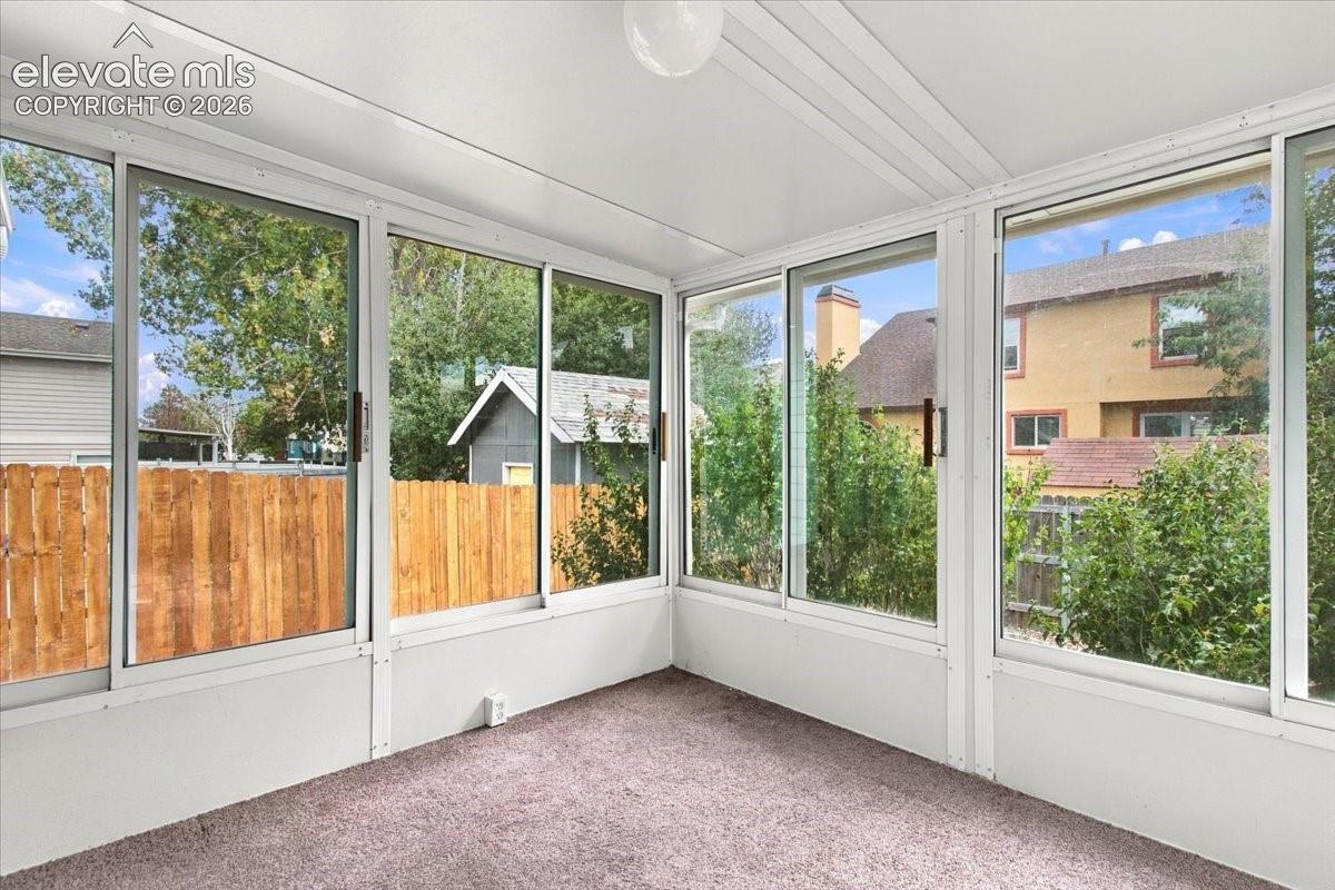 Sunroom featuring multiple floor-to-ceiling sliding glass windows, white structural framing, and neutral carpeting