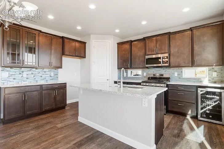 Kitchen featuring dark wood cabinetry, an island with a stone-composite countertop, mosaic tile backsplash, wood-finish flooring, and a built-in beverage refrigerator