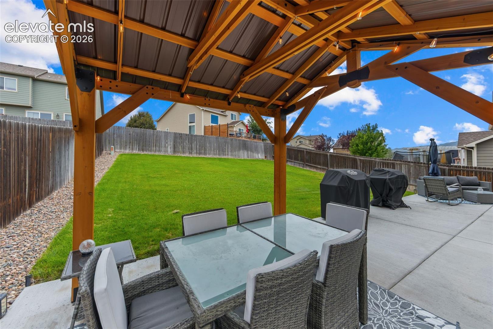 Patio featuring a wood pergola with a metal roof, concrete hardscaping, and a lush green lawn