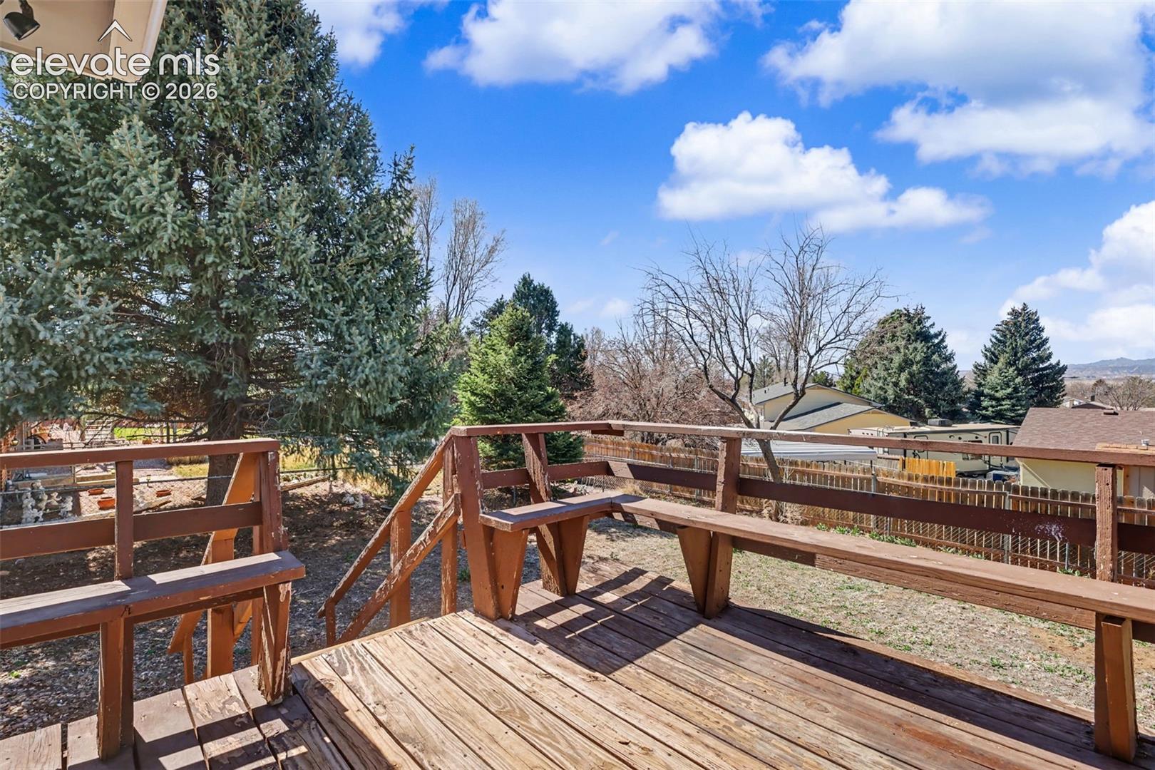 Elevated wood deck featuring built-in bench seating, wood railings, and stairs leading to the yard, complemented by mature evergreen trees