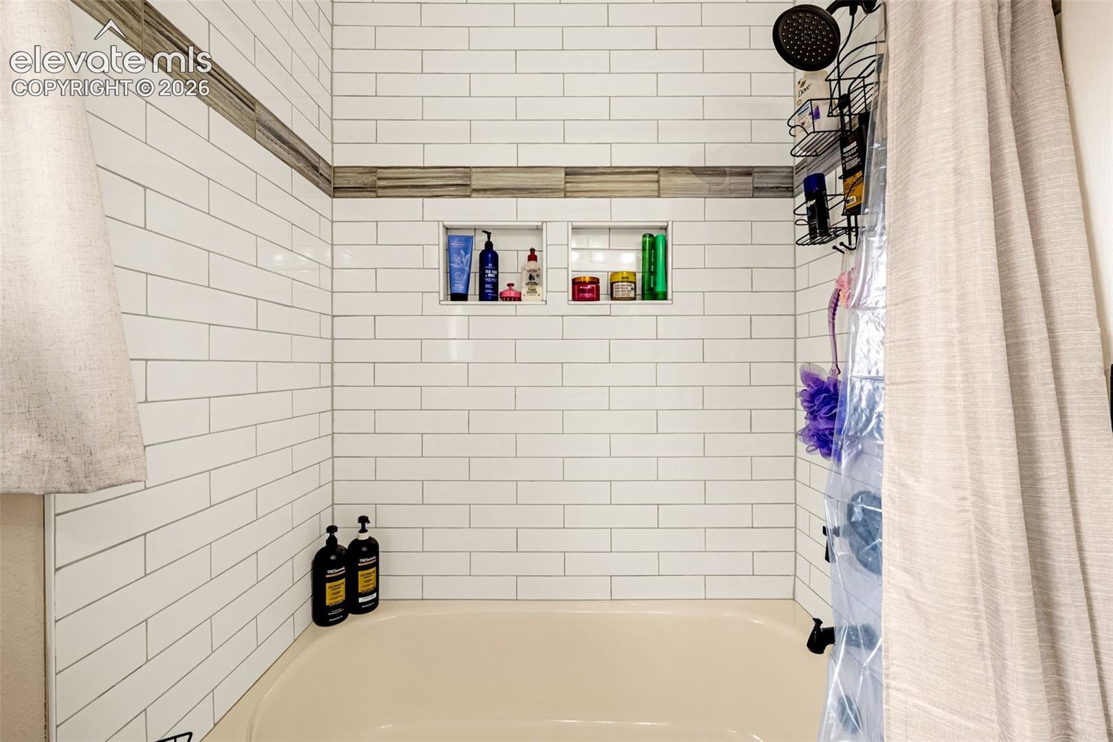 Shower surround featuring white subway tile, a neutral-toned decorative accent border, and dual recessed wall niches