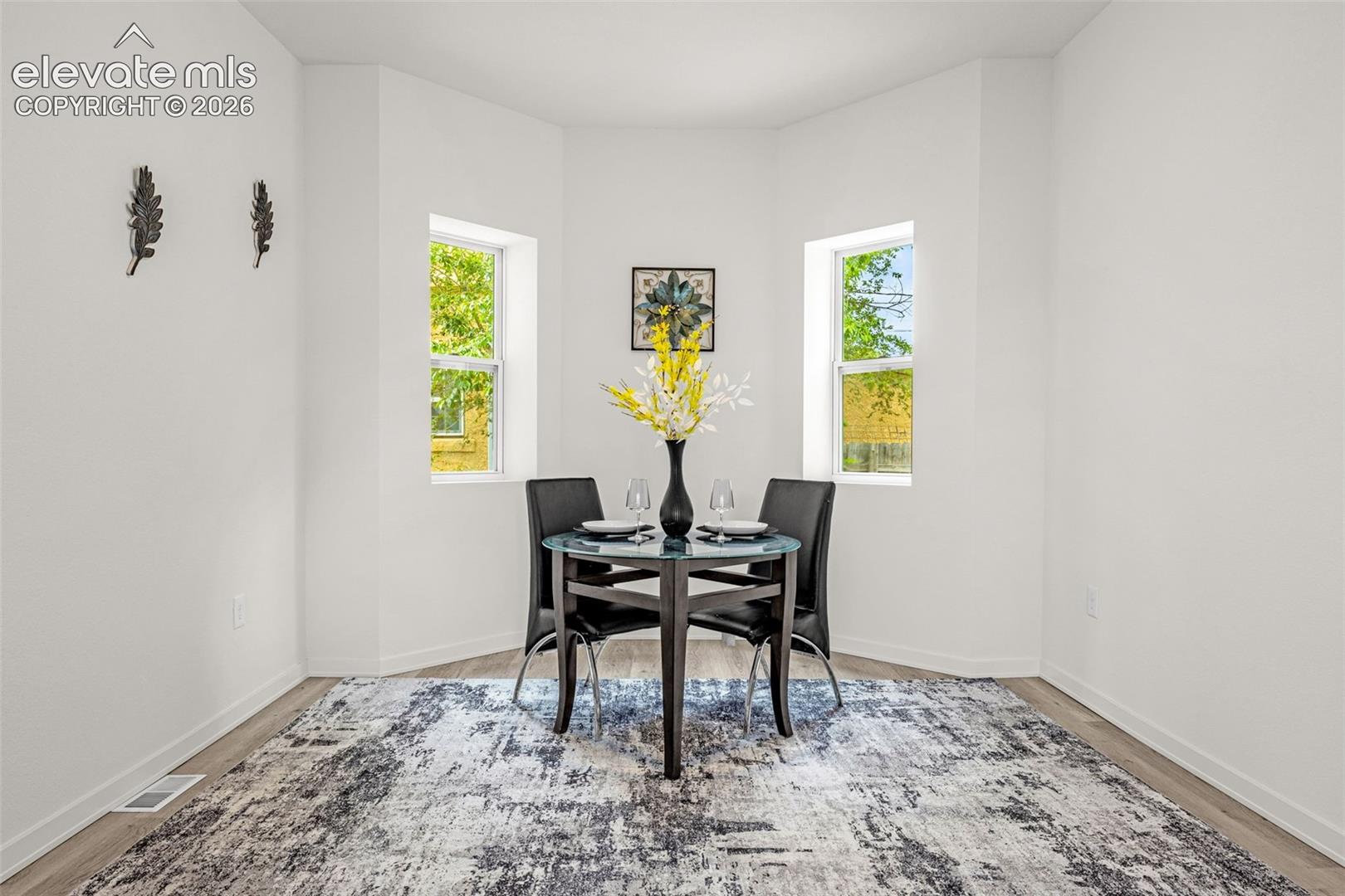 Bright dining nook featuring two windows, wood-finish flooring, and crisp white walls